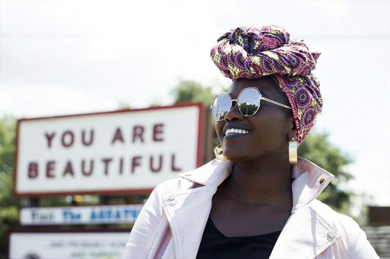 autoconfiança mulher negra sorrindo olhando para o horizonte. Placa escrito "You are beautiful" ao fundo. 