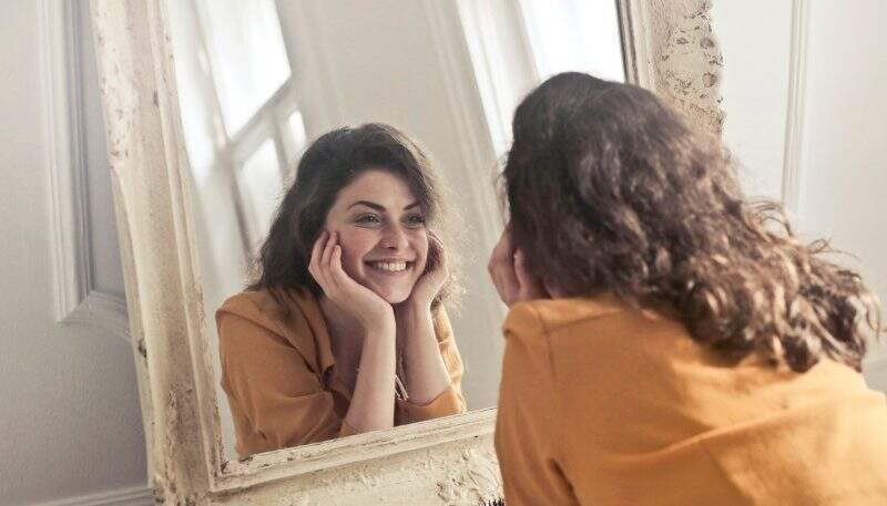 Saúde emocional mulher se olhando no espelho e sorrindo